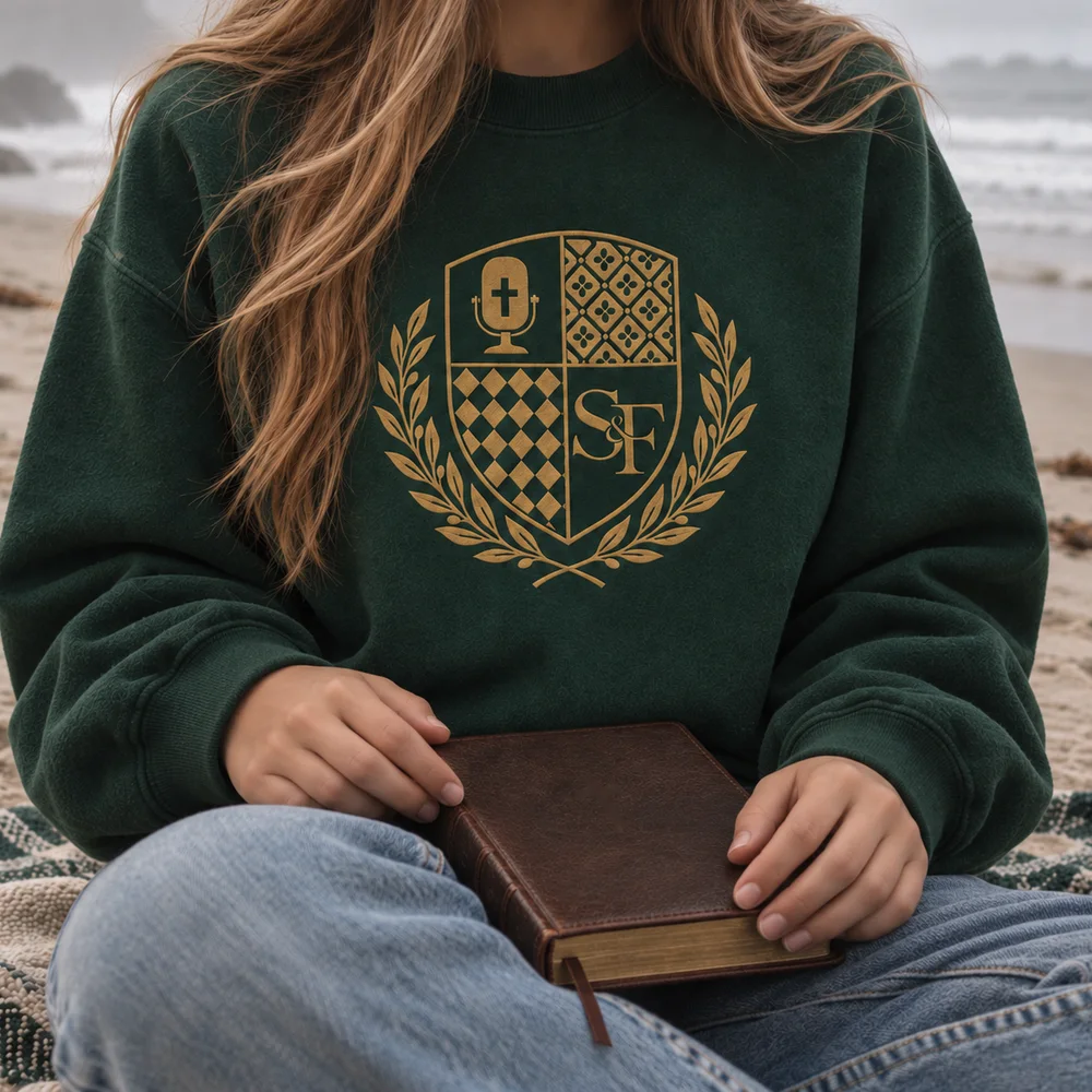 Salt&Found embroidered crest crewneck in forest green, worn on a misty beach with a leather Bible