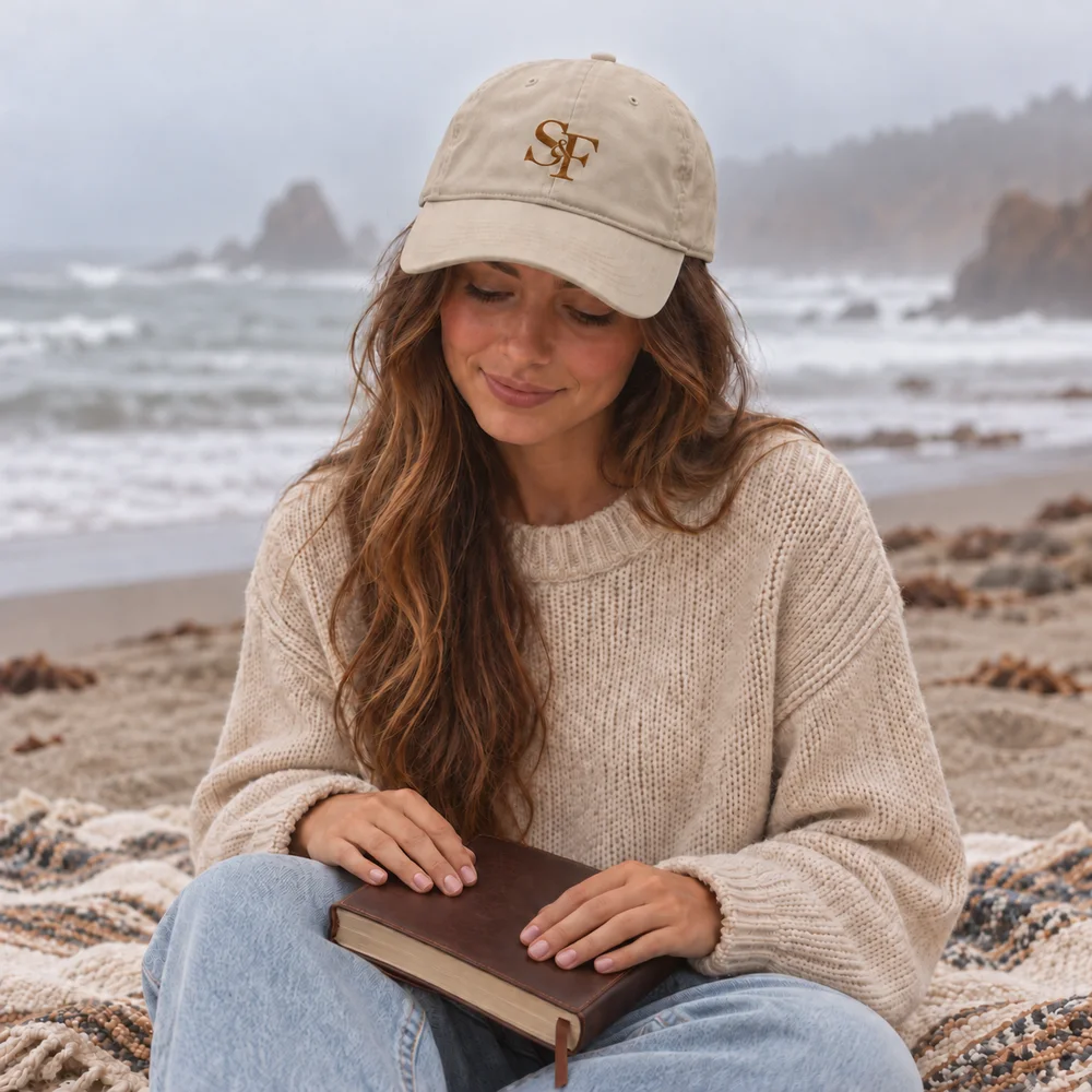 Salt&Found monogram dad hat in cream with gold thread, worn on a misty beach with a leather Bible